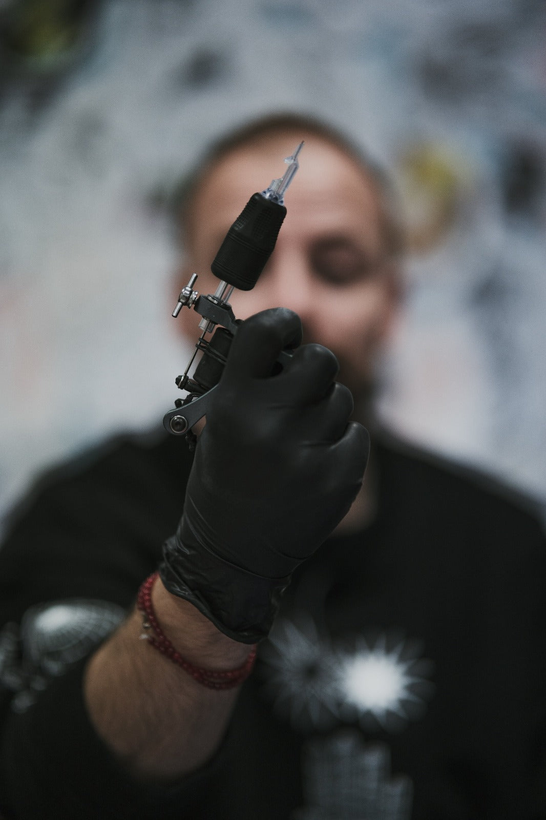 Tattoo artist holding a modern rotary tattoo machine in a gloved hand, with a blurred background