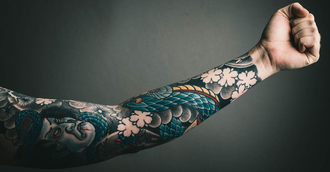Tattooed arm raised in a flexing pose, showcasing colorful black and ivory black ink designs