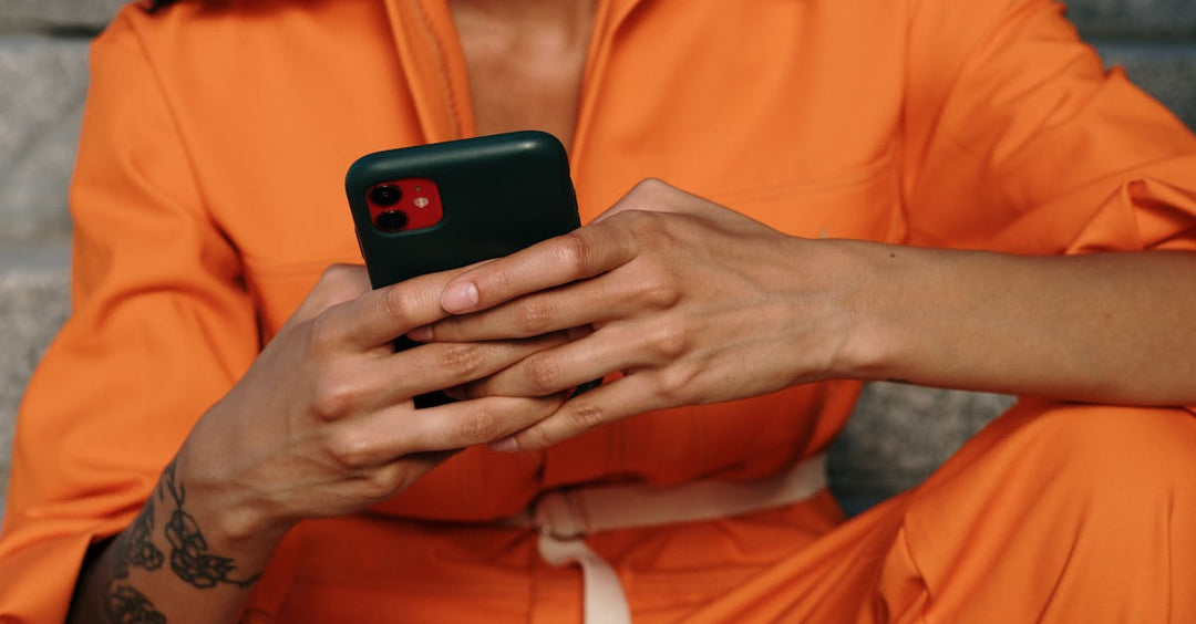 Tattooed person in orange outfit holding a wireless device, symbolizing mobility and modern equipment