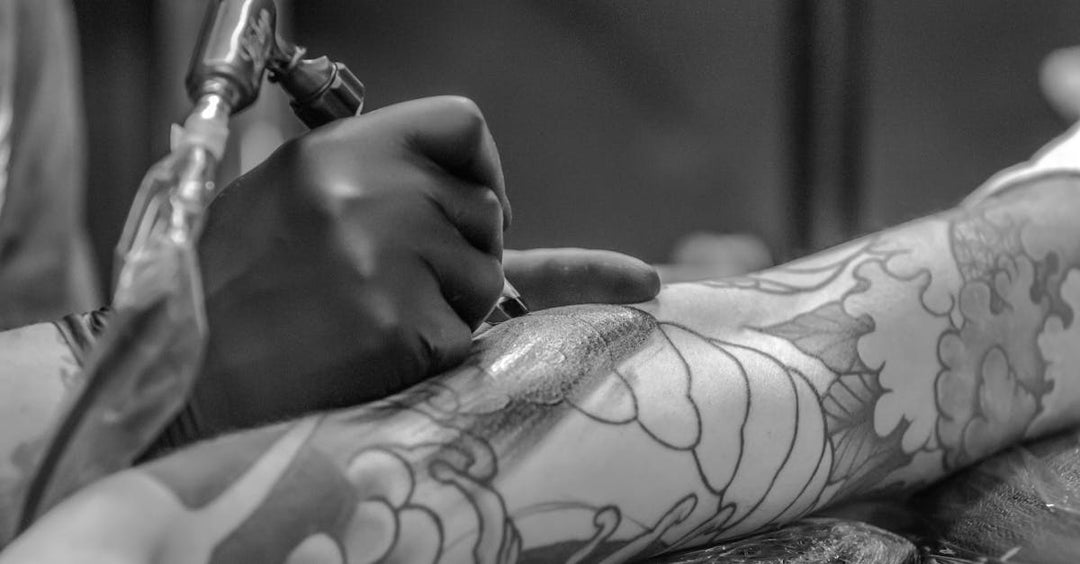 Tattoo artist using a rotary machine to ink a detailed arm design in a professional setting